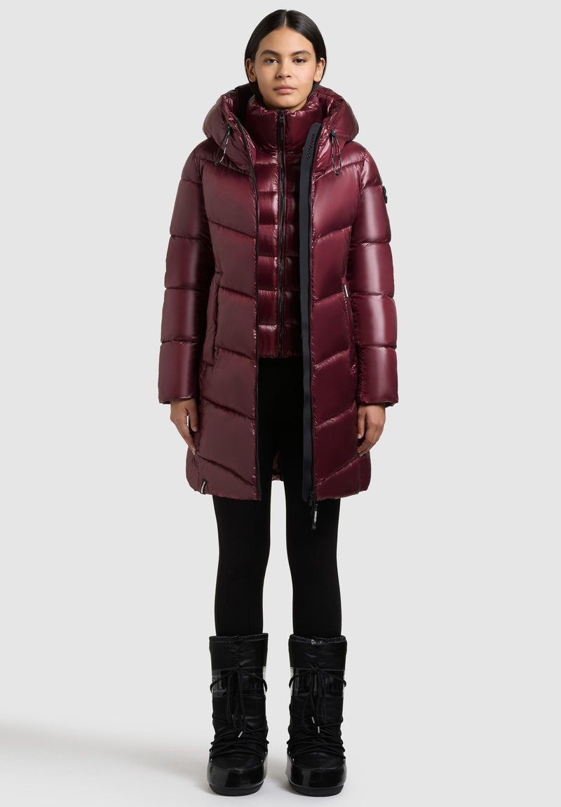 Bordo zimska jakna s kapucom, s patentnim zatvaračem sprijeda, kvadratnim uzorkom i crnim detaljima. Crne zimske čizme dovršavaju outfitu.