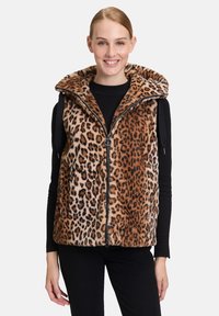 Kamizelka w panterkę z wysokim kołnierzem, wykonana z miękkiego sztucznego futra, z przednim zamkiem błyskawicznym i dwoma bocznymi kieszeniami. Paleta kolorów obejmuje odcienie brązu i beżu.