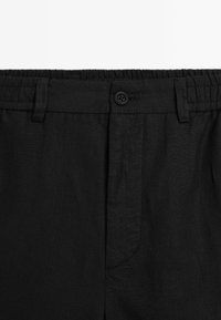 Pantaloni in lino neri con vita elastica, chiusura a bottone e tasche laterali con cuciture rifinite. Texture liscia.