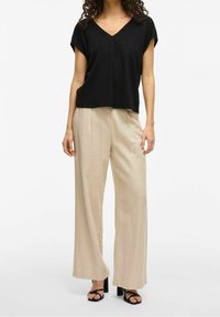 Haut noir à col en V avec manches courtes et coupe décontractée, associé à un pantalon beige à jambes larges avec une texture douce et un pli central. Sandales à talons noires.