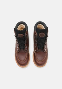 Botas de couro castanho com gola em tecido preto, bico arredondado e sola em tom contrastante. Apresenta cordões pretos e detalhes cosidos.