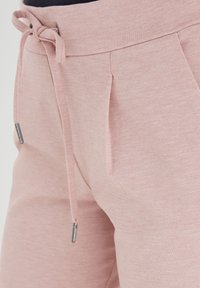 Jasnoróżowe dresy z teksturowanej tkaniny, elastycznym pasem w talii z sznurkiem oraz bocznymi plisami, zapewniającymi luźny krój.