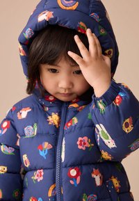 Kolorowa pikowana kurtka z granatowym tłem ozdobiona wzorami zwierząt i kwiatów, zamkiem błyskawicznym i kapturem.