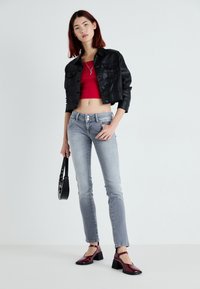 Jaqueta de couro preta cropped, top vermelho cropped, jeans slim-fit cinza claro, sapatos de salto bloco cor burgundy, segurando uma pequena bolsa preta.