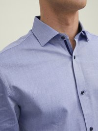 Camicia azzurra a fantasia con colletto strutturato, caratterizzata da bottoni scuri e un tessuto testurizzato. La vista ravvicinata mostra le cuciture dettagliate.