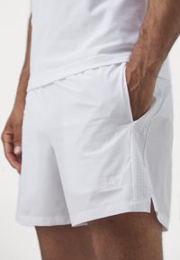 Pantalones cortos deportivos blancos hechos de un material ligero, con un patrón de rejilla en el costado, un logo en el dobladillo y un bolsillo en ángulo.