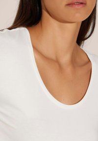 Witte katoenen blouse met een brede ronde halslijn, met een gladde textuur en een getailleerd ontwerp, dat het sleutelbeen accentueert.