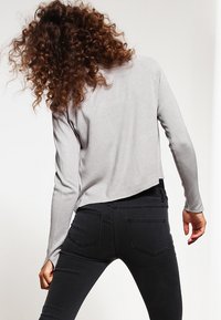 Šedý zkrácený top s dlouhým rukávem a žebrovanou strukturou. Černé přiléhavé džíny s zadními kapsami. Oba kusy mají neformální, moderní design.