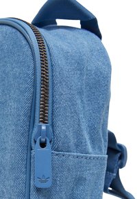 Zaino in denim blu con una superficie texture, dotato di una zip scura a contrasto e un tirazip blu con branding.