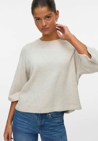 Hele beež keeratud sviiter ümmarguse kaeluse, 3/4-sleeve'ide ja lõdva lõikega, koos siniste teksadega. Pehme tekstuur ja minimaalne disain.