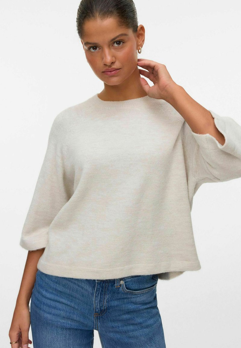 Hele beež keeratud sviiter ümmarguse kaeluse, 3/4-sleeve'ide ja lõdva lõikega, koos siniste teksadega. Pehme tekstuur ja minimaalne disain.