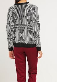 Svart och vit stickad tröja med geometriskt mönster, randig textur och ribbade ärmslut. Tillsammans med mörkröda byxor.