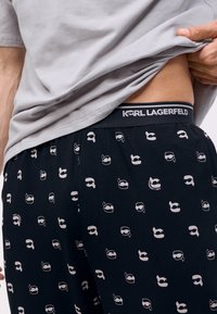 Čierne pyžamové nohavice s opakujúcim sa svetloružovým vzorom rôznych ilustrovaných tvárí. Elastický pás zdobí text "KARL LAGERFELD".