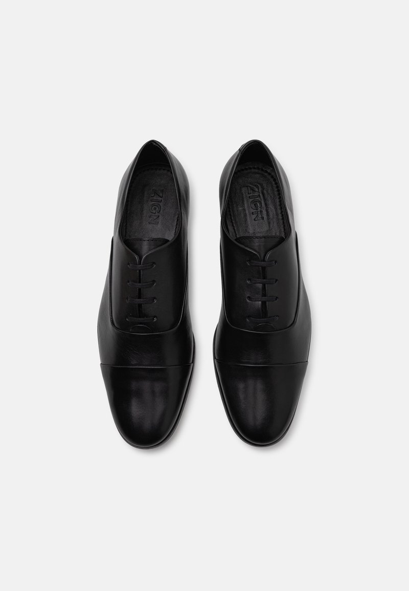 Schwarze Leder Schuhe mit glatter Oberfläche, runder Zehenform, Schnürdesign und einem kontrastierenden Kappenzehenelement. Flache Sohle, minimalistisches Design.