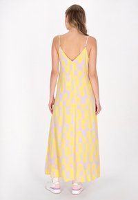 Maxikleid mit V-Ausschnitt-Design. Gelber Stoff mit großen lavendelfarbenen geometrischen Mustern. Leichtes, fließendes Material. Verstellbare Träger.