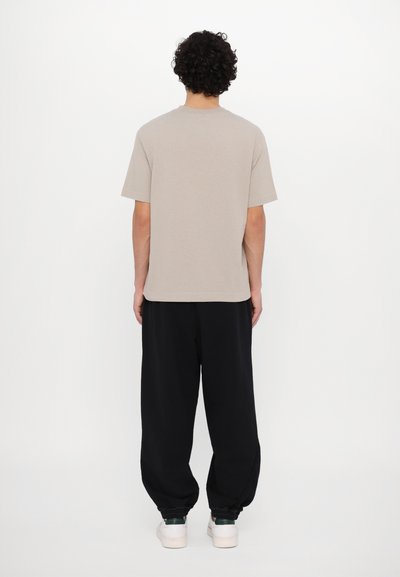 Beige cotton t-shirt with a crew neckline, short sleeves, and relaxed fit, paired with black sweatpants and white sneakers.