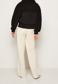 Czarna polarowa kurtka z teksturowanym tyłem, zestawiona z kremowymi spodniami z szerokimi nogawkami z korduroju. Kurtka posiada prążkowane mankiety i dół.