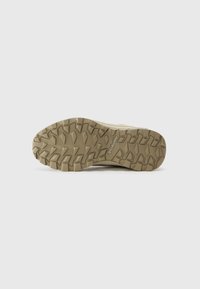 Semelle de chaussure de randonnée marron clair avec des crampons épais et robustes. Présente un dessous texturé pour une meilleure adhérence et un logo en relief près du talon.