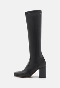 Botte noire montant en cuir lisse, dotée d'un bout carré, d'un épais talon bloc et d'un design minimaliste avec de subtils accents de couture.