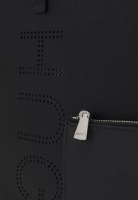 Tessuto nero testurizzato con testo perforato "HUGO" e una cerniera argentata con inciso "HUGO" su una piccola tasca.