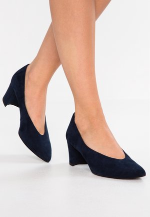 Chaussures à talons en daim bleu marine avec un bout pointu et un design découpé en forme de V, dotées d'un talon épais et carré pour plus de stabilité.