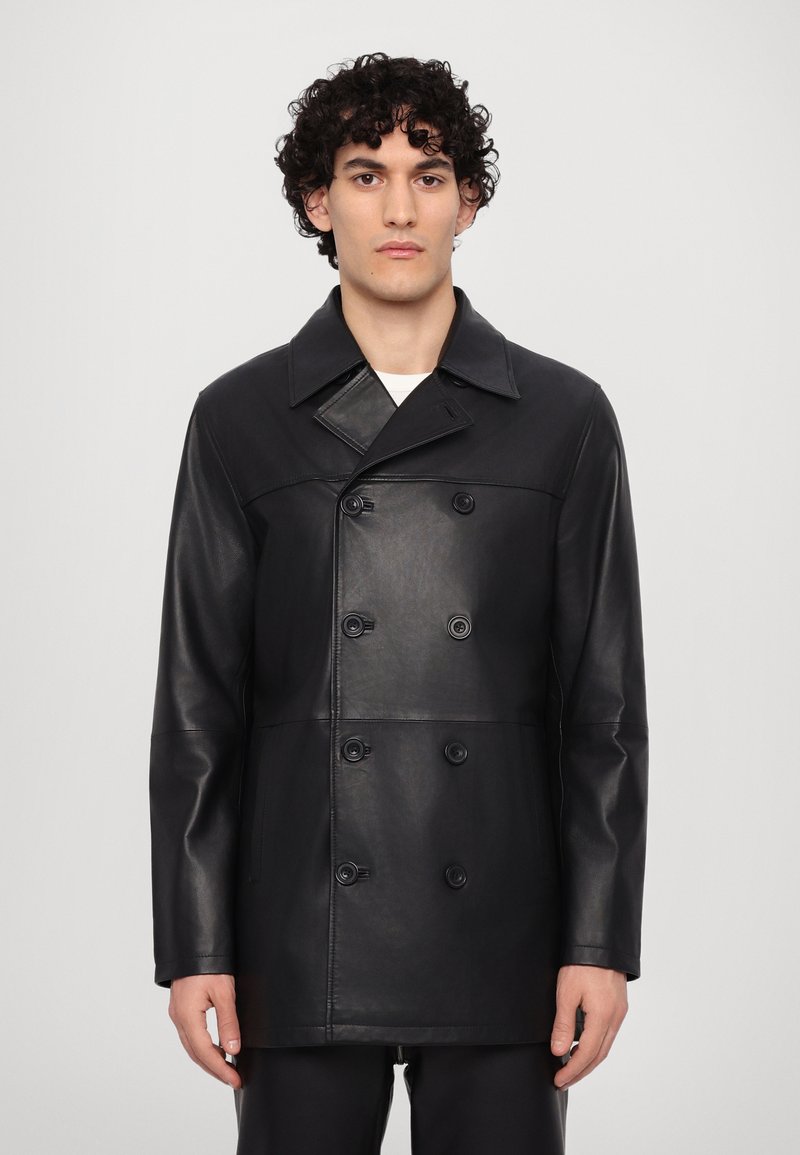 Manteau noir croisé en cuir. Presentant un large col, deux rangées de boutons et une texture lisse avec un minimum de détails.