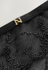 Black lace lingerie with floral embroidery, featuring a satin waistband and a gold "N" logo accent at the top. Textured and delicate design.