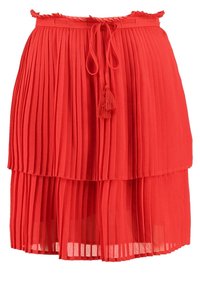 Falda plisada roja con diseño en capas, cintura con lazo y terminales de borlas, hecha de una tela ligera y semitranslúcida.