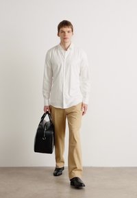 Weißes Hemd mit Knöpfen, beige Hose, schwarze Schuhe und eine schwarze Tasche. Glatter Stoff, taillierte Passform, mit einem minimalistischen Design.
