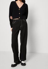 Cárdigan negro de punto con escote en V y cierre de botones, combinado con pantalones negros de pierna ancha que cuentan con acentos de costura blanca. Zapatos gruesos en blanco y negro.