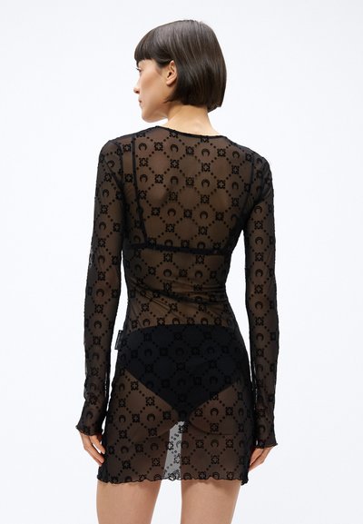 Čierne priehľadné šaty s dlhým rukávom s kvetinovým vzorom, so zaobleným lemom a priliehavým strihom, vrstvené na pevných čiernych nohaviciach.