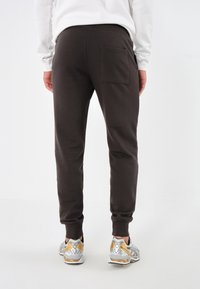 Braune Sweatpants aus Baumwollmischung, ausgestattet mit einer Gesäßtasche, schmal zulaufenden Beinen und gerippten Bündchen, kombiniert mit silbernen und goldenen Sportschuhen.