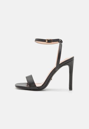 Sandale à talon haut noire au design élégant, dotée d'une fine bride de cheville, de deux larges brides sur le pied et d'une finition brillante.