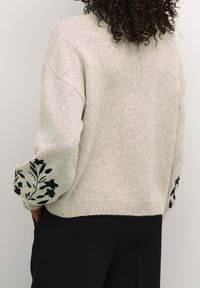 Sweatshirt en tricot gris clair avec de longues manches amples, ornées d'une broderie florale foncée au niveau des poignets. Texture douce et design à ourlet droit.