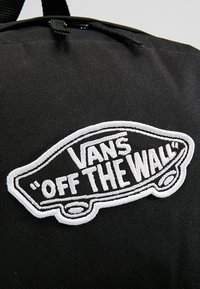 Sac à dos en tissu noir avec un patch logo Vans "Off The Wall" de skateboard brodé en blanc.