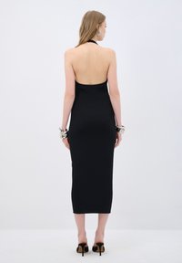 Abito midi nero a costine con scollatura a halter e schiena scoperta, caratterizzato da una silhouette aderente e abbinato a bracciali argento chunky e tacchi neri.