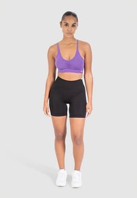 Lila sport-bh med rynkning i mitten, kombinerad med svarta högmidjade korta leggings. Vita sneakers fullbordar outfiten.