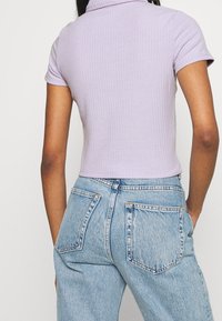 Top de manga corta acanalado en color lila con cuello tipo polo, combinado con jeans de mezclilla azul claro de cintura alta, que tienen bolsillos traseros y un corte relajado.