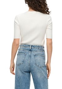 Witte geribbelde gebreide top met korte mouwen, gecombineerd met lichtblauwe denim jeans met hoge taille, voorzien van twee achterzakken en een vervaagde was.