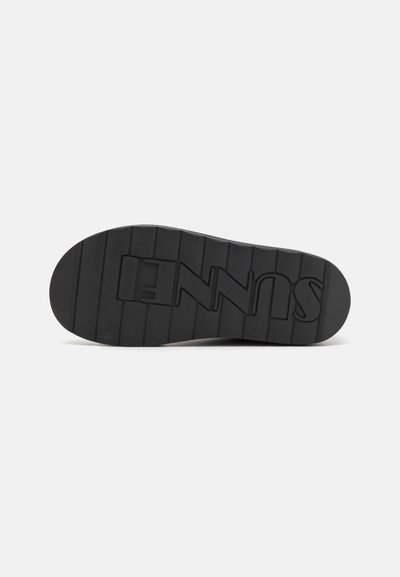 Talpa de pantof din cauciuc negru cu nervuri orizontale și logo. Formă plată, suprafață texturată și design cu vârf rotunjit.