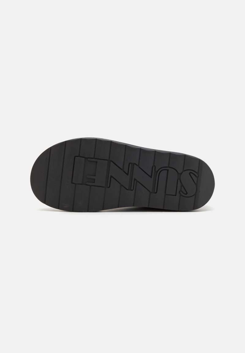 Black rubber shoe sole with horizontal ridges and logo. Flat shape, textured surface, and rounded toe design.