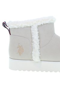 Helle beige Knöchelstiefel mit weißen Kunstfellbesätzen, Zuglasche mit rot-blauen Streifen und geprägtem Polo-Spieler-Logo an der Ferse.
