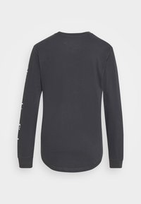 Langærmet sort t-shirt lavet af bomuld, med rund hals og en buet kant. Venstre ærme har hvid grafisk detaljer.