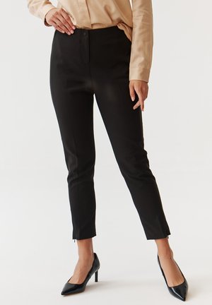 Black tailored pants with a mid-rise waist, slim fit, and side zip. Material appears smooth with no visible patterns. Paired with black heels.