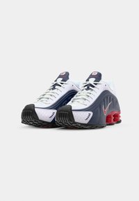 Nike tenisice imaju bijeli, perforirani gornji dio s tamnoplavim akcentima, crvenim detaljima na potplatu i prepoznatljivim dizajnom ublaženog potplata.