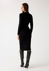 Abito midi nero a coste con maniche lunghe, silhouette aderente e scollatura rotonda, abbinato a stivali neri con tacco al ginocchio.