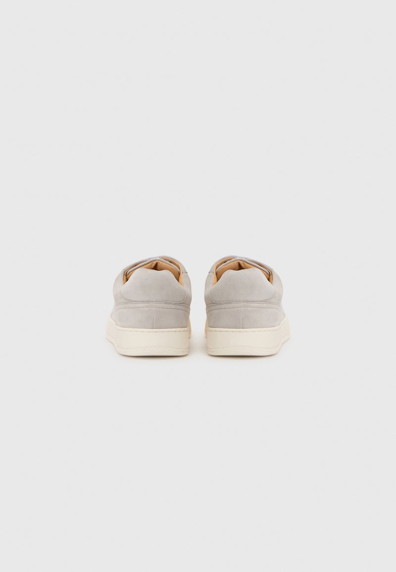 Baskets en daim gris à profil bas, avec une semelle en caoutchouc blanche cassée contrastante et de simples accents cousus au niveau du talon.