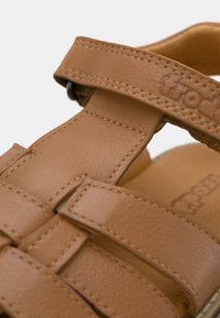 Καφέ δερμάτινο σανδάλι με πολλαπλούς διασταυρούμενους ιμάντες, υφή επιφάνειας και αντίθετες ραφές. Ορατή μαλακή εσωτερική σόλα.