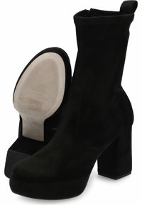 Botines de ante negro con tacones de bloque y cremalleras laterales, mostrando una bota con suela texturizada en beige y detalles de tamaño.