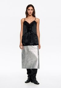Czarna satynowa halka z koronkową lamówką i wiązaniami, zestawiona ze srebrną metaliczną spódnicą midi, noszona z czarnymi luźnymi botkami.